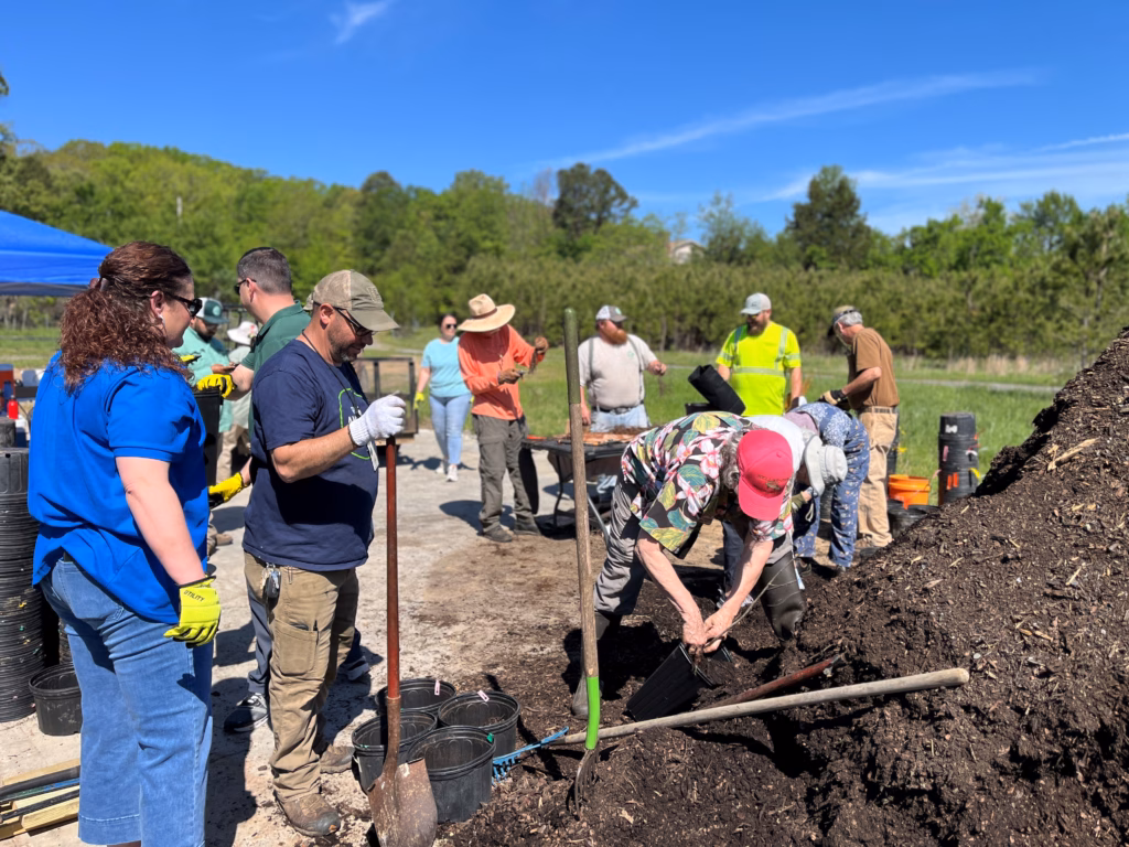 People are standing around a large pile of soil, preparing to plant tree seedlings.